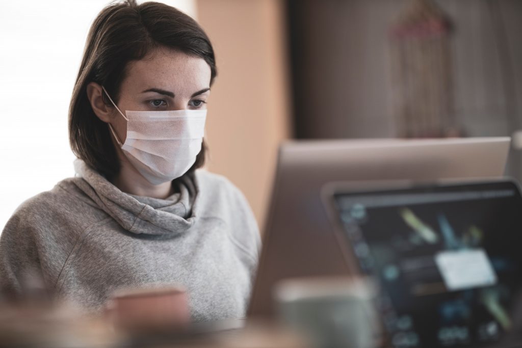 Image ID: a young woman wearing a mask at her computer in a home office environment